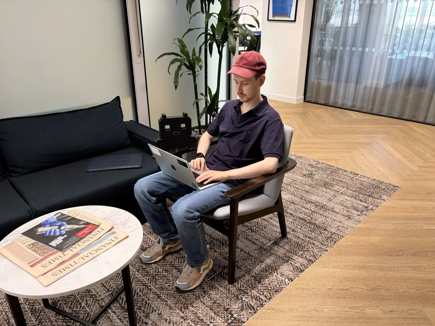 A printed OpenAPPA mascot sitting on a sofa behind a developer working on a laptop